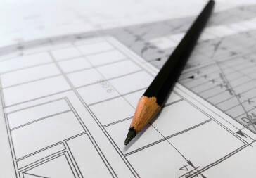 Black pencil resting on black and white blueprint